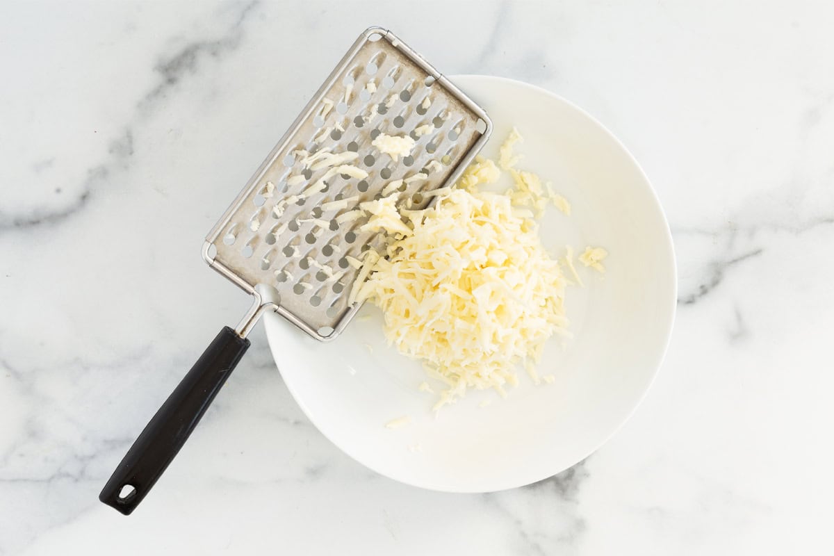 Grating cheese into white bowl for cheese sauce for pretzels.