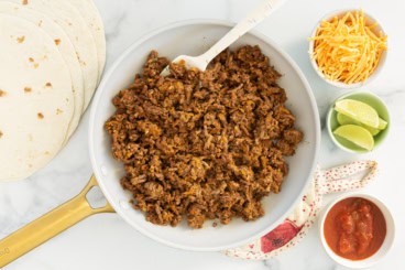 Taco meat in pan with taco supplies on side.