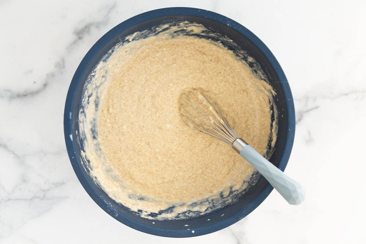 Batter for oatmeal protein pancakes in blue bowl with whisk.