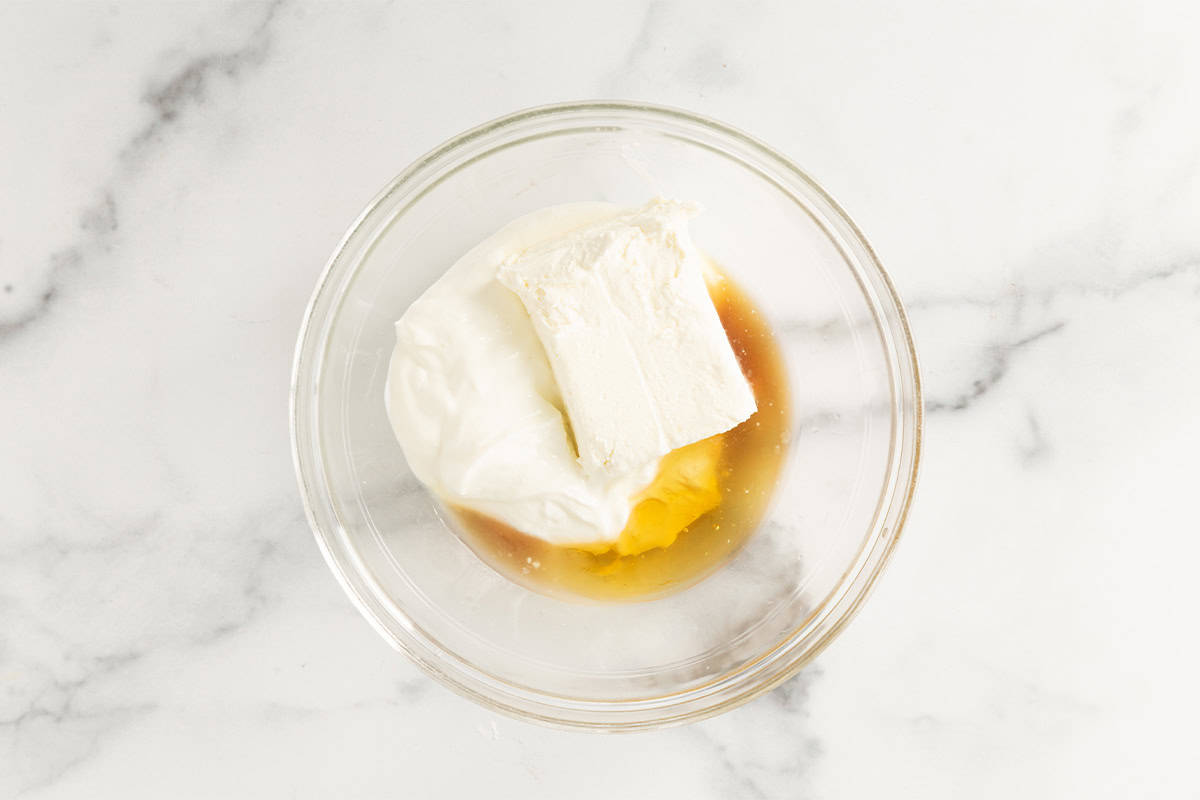 Ingredients for cheesecake dip in glass bowl before mixing.