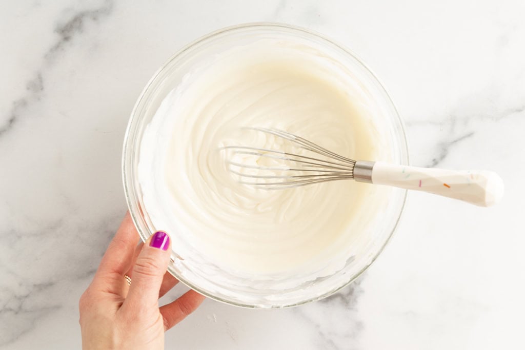 Cheesecake dip in glass bowl with whisk.