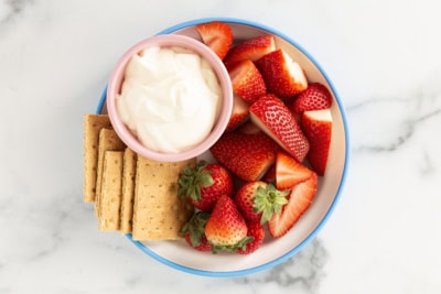 Cheesecake dip with fruit and crackers on plate.