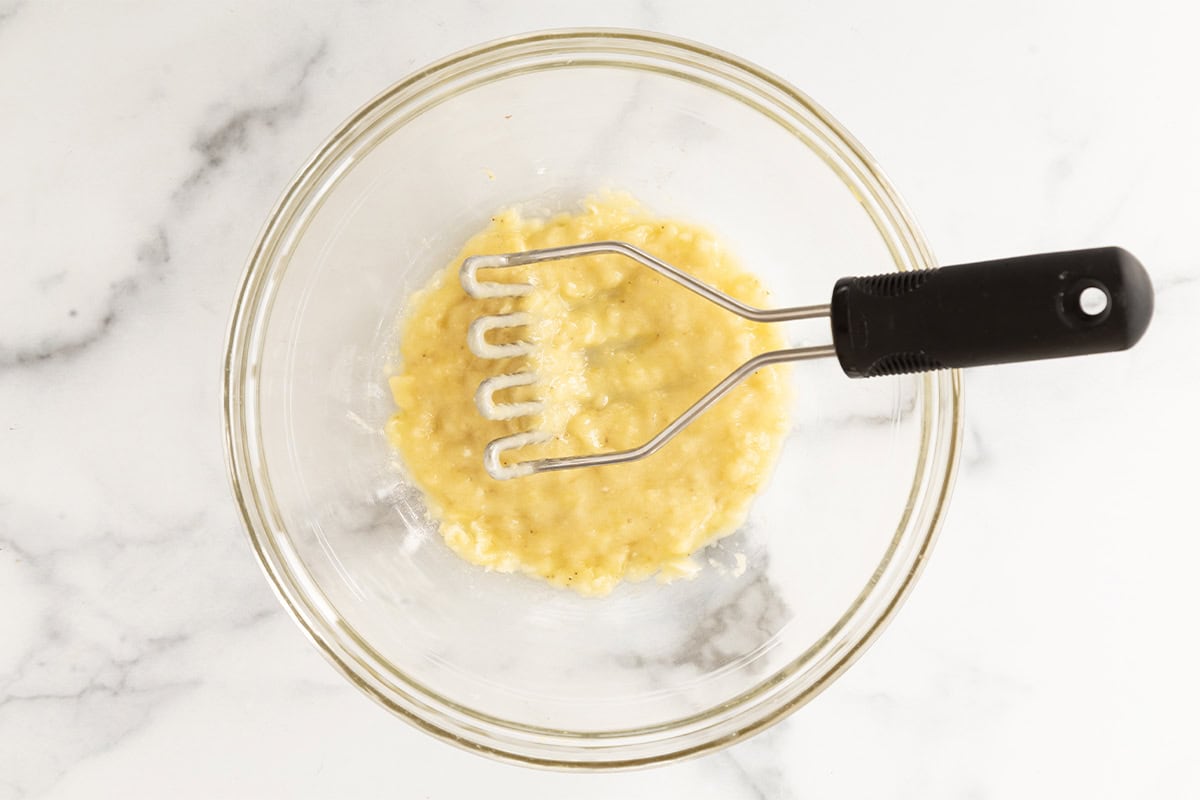 Banana being mashed in glass bowl for chocolate snack cake.