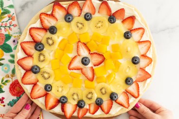 Hands holding fruit pizza.