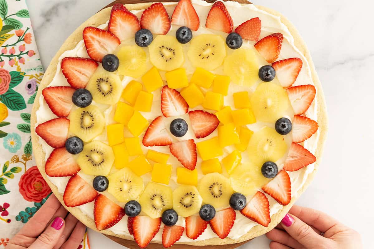 Hands holding fruit pizza. 