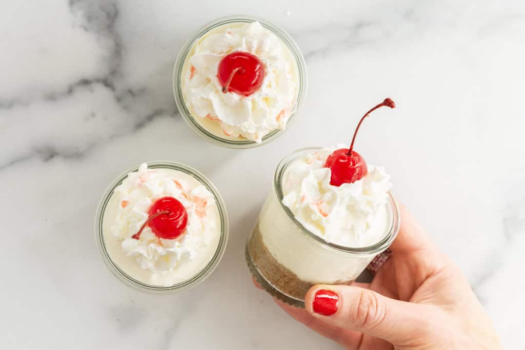 Three cheesecake cups with hand holding one.